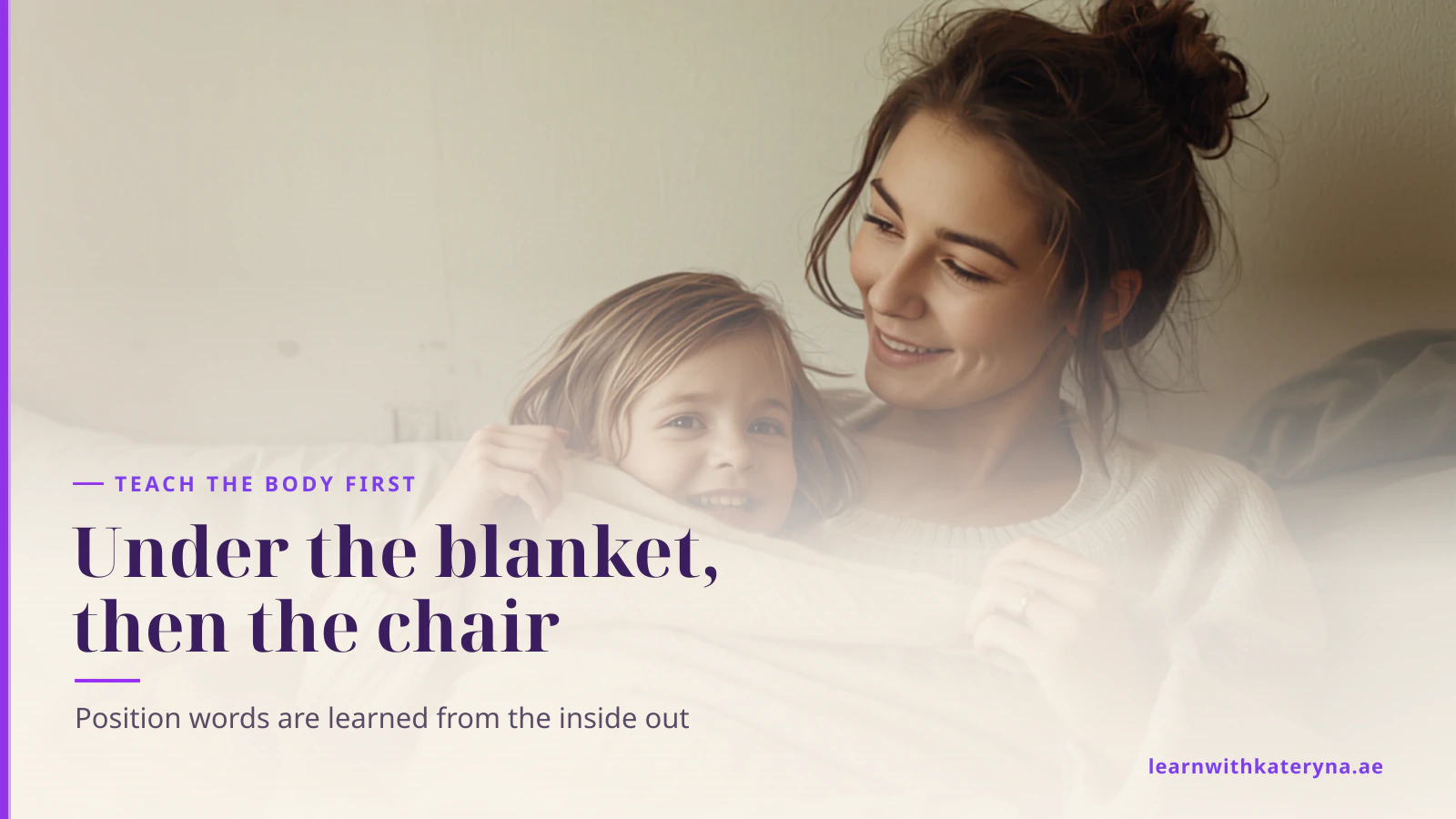 A toddler holds a blanket up over herself, laughing, while her mother speaks to her