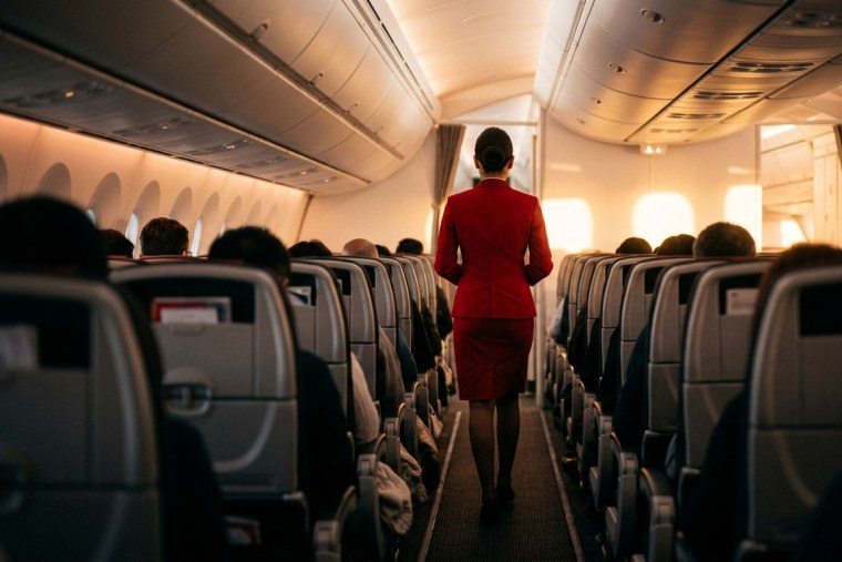 Бортпровідниця Emirates у червоній формі йде проходом літака до світла